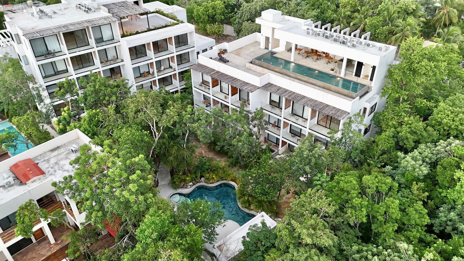 Aerial view of Erena Mindful Apartments, La Veleta, Tulum, showing its rooftop infinity pool and ground-level courtyard pool