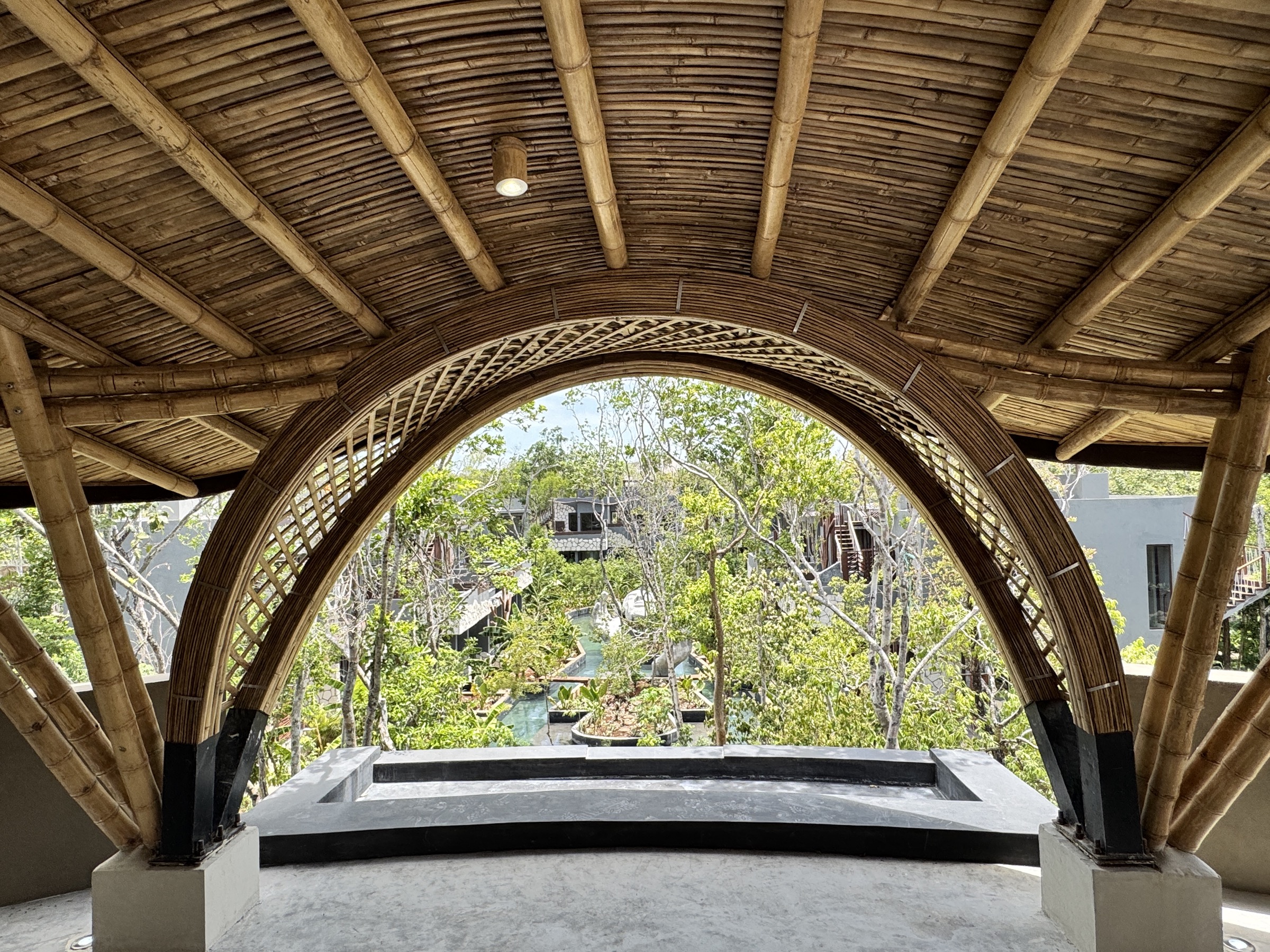 Bamboo-arched pavilion opening onto the canal pools at Siwá Élevé, jungle canopy beyond
