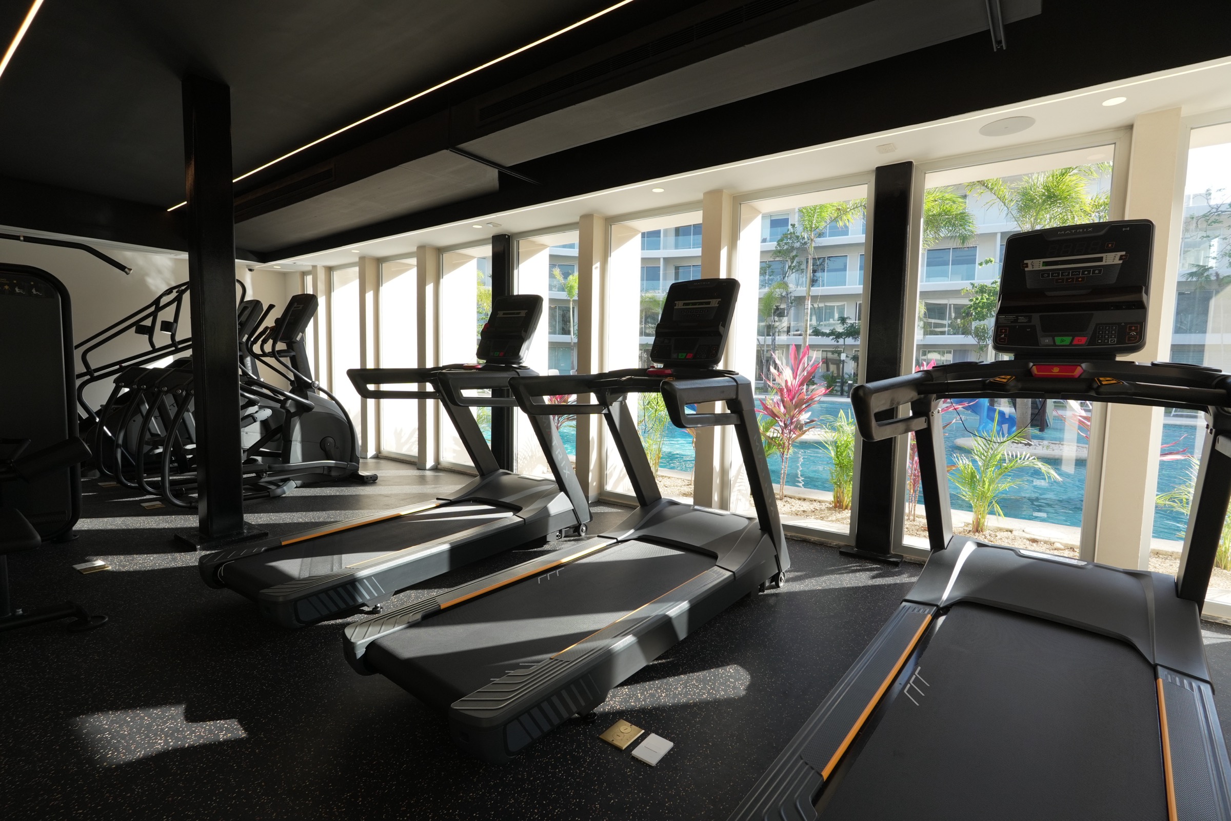 Gym at The Leaf Condos Playacar with treadmills facing a glass wall onto the pool